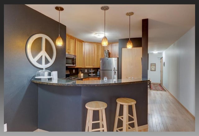 kitchen featuring pendant lighting, stainless steel appliances, light brown cabinets, kitchen peninsula, and light wood-type flooring