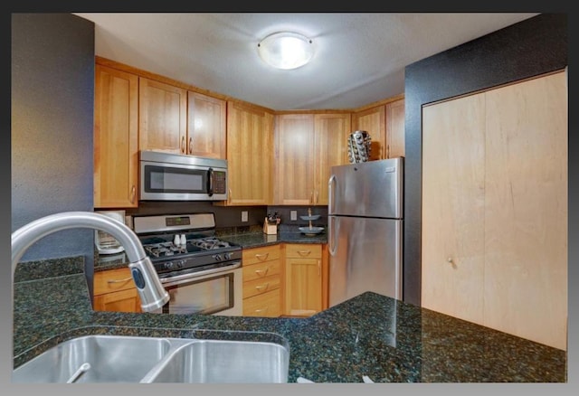 kitchen featuring appliances with stainless steel finishes, sink, light brown cabinetry, and dark stone counters