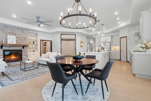 dining space featuring ceiling fan, light wood-type flooring, built in features, a fireplace, and a tray ceiling