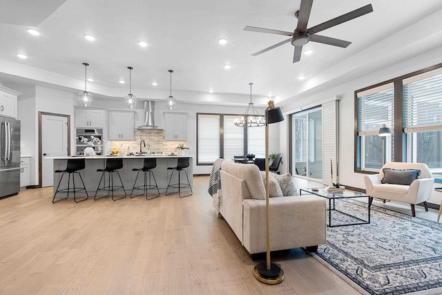 living room with a wealth of natural light, light hardwood / wood-style flooring, ceiling fan with notable chandelier, and sink