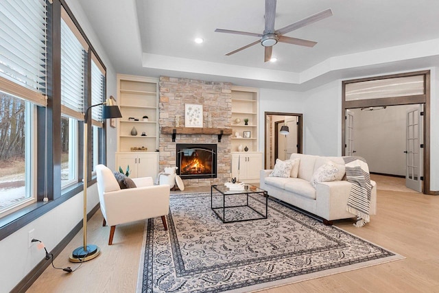 living room with hardwood / wood-style floors, a stone fireplace, built in features, and a wealth of natural light