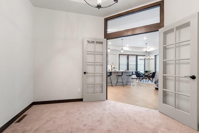 carpeted spare room featuring french doors and a chandelier