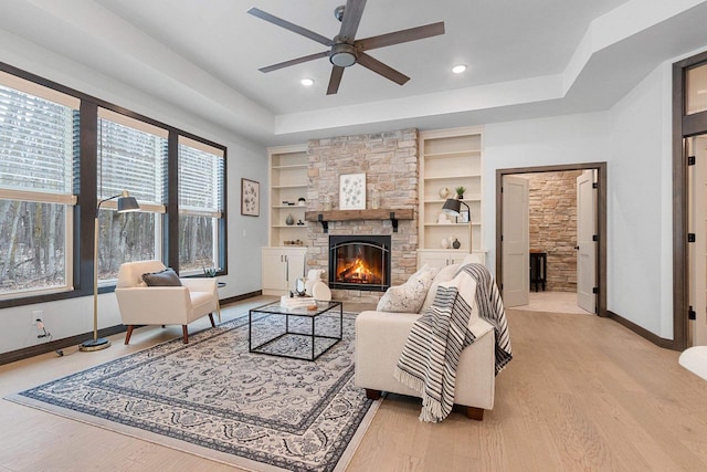 living room with ceiling fan, a stone fireplace, built in features, and light hardwood / wood-style flooring