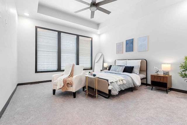 bedroom with ceiling fan, light carpet, and a tray ceiling