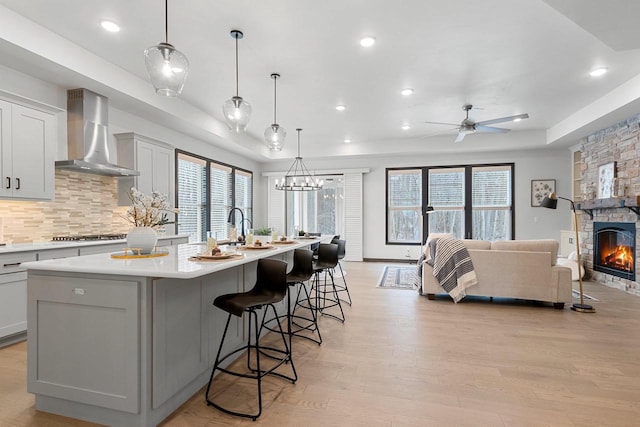 kitchen with wall chimney exhaust hood, ceiling fan, hanging light fixtures, and a large island with sink