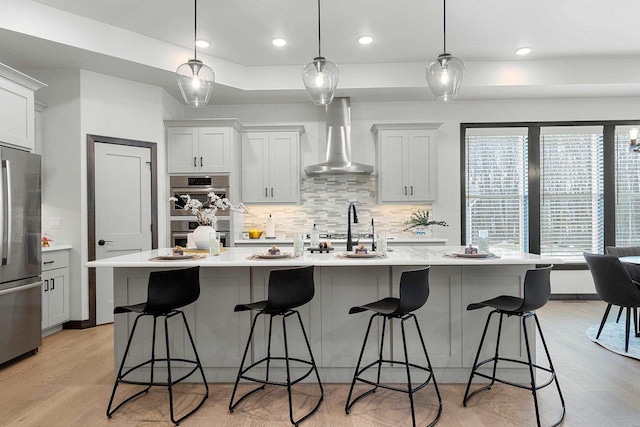 kitchen with tasteful backsplash, stainless steel appliances, a spacious island, wall chimney range hood, and pendant lighting