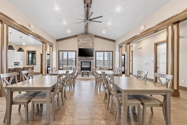 dining space featuring ceiling fan, high vaulted ceiling, beamed ceiling, light hardwood / wood-style floors, and a stone fireplace