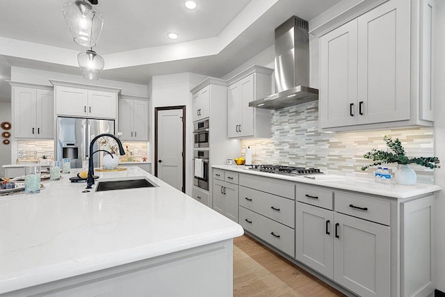 kitchen with sink, stainless steel appliances, hanging light fixtures, wall chimney range hood, and decorative backsplash