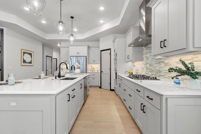 kitchen with wall chimney range hood, sink, tasteful backsplash, decorative light fixtures, and stainless steel appliances