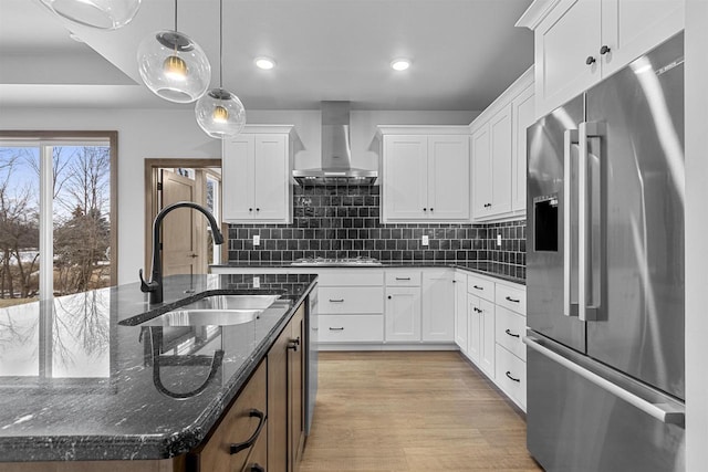 kitchen with appliances with stainless steel finishes, sink, wall chimney range hood, decorative light fixtures, and white cabinets