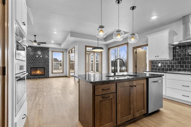 kitchen with white cabinetry, sink, a tiled fireplace, decorative backsplash, and a center island with sink