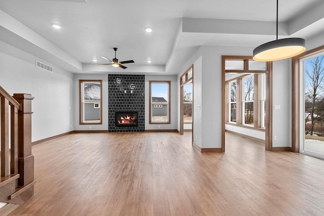 unfurnished living room featuring ceiling fan, a raised ceiling, light wood-type flooring, and a tiled fireplace