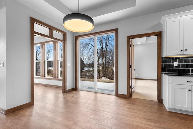 doorway to outside with plenty of natural light, light wood-type flooring, and a tray ceiling