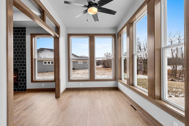 unfurnished sunroom with plenty of natural light, ceiling fan, and a tile fireplace