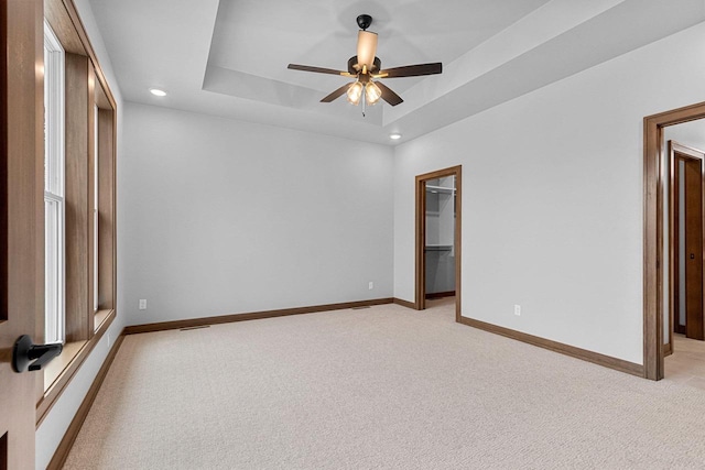 carpeted spare room with a raised ceiling and ceiling fan