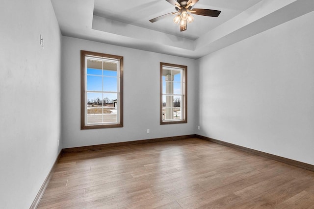 empty room featuring ceiling fan, a raised ceiling, and light wood-type flooring