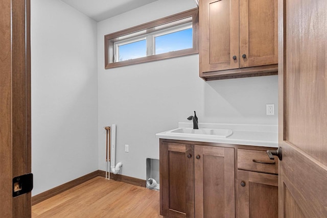 laundry room featuring cabinets, light hardwood / wood-style flooring, and sink