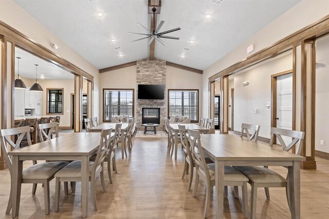 dining room featuring ceiling fan, beam ceiling, high vaulted ceiling, a fireplace, and light hardwood / wood-style floors