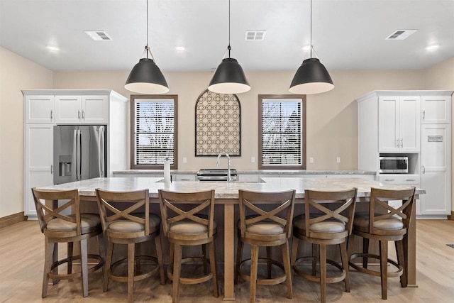 kitchen featuring appliances with stainless steel finishes, decorative light fixtures, white cabinetry, and a large island with sink