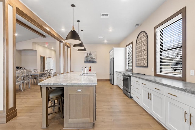 kitchen with light stone countertops, stainless steel appliances, decorative light fixtures, a center island with sink, and white cabinets