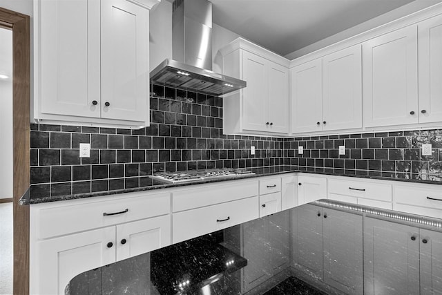 kitchen with stainless steel gas stovetop, white cabinets, wall chimney range hood, decorative backsplash, and dark stone countertops