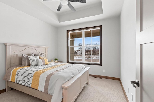 bedroom featuring ceiling fan, light colored carpet, and a tray ceiling