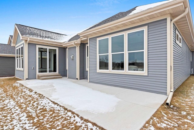 snow covered rear of property with a patio area