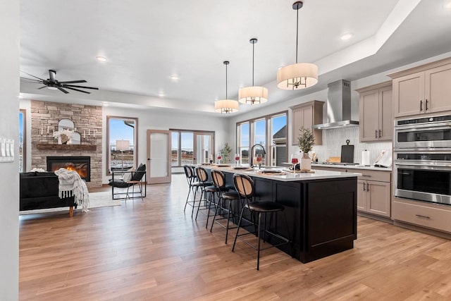 kitchen with a breakfast bar, a kitchen island with sink, wall chimney range hood, pendant lighting, and a fireplace