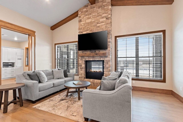 living room with beamed ceiling, high vaulted ceiling, light hardwood / wood-style floors, and a stone fireplace