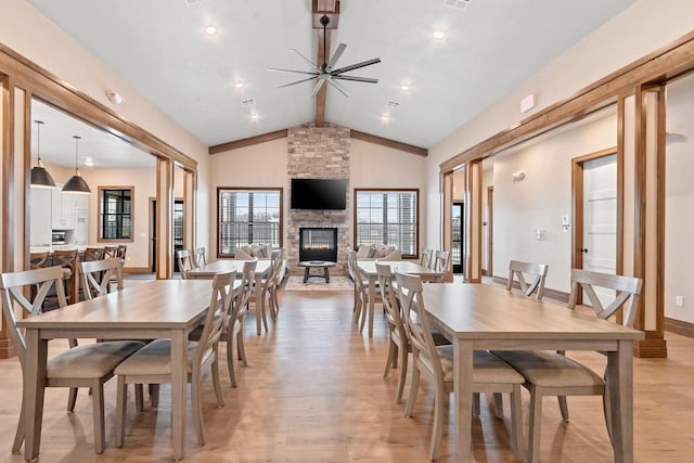 dining space featuring light wood-type flooring, ceiling fan, high vaulted ceiling, beamed ceiling, and a stone fireplace