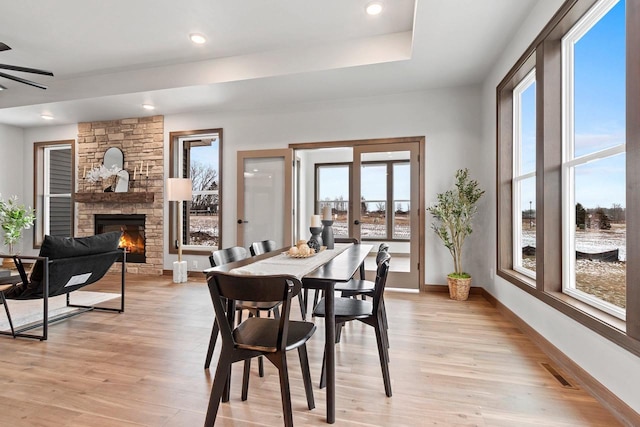 dining area with ceiling fan, a healthy amount of sunlight, a stone fireplace, and light hardwood / wood-style floors