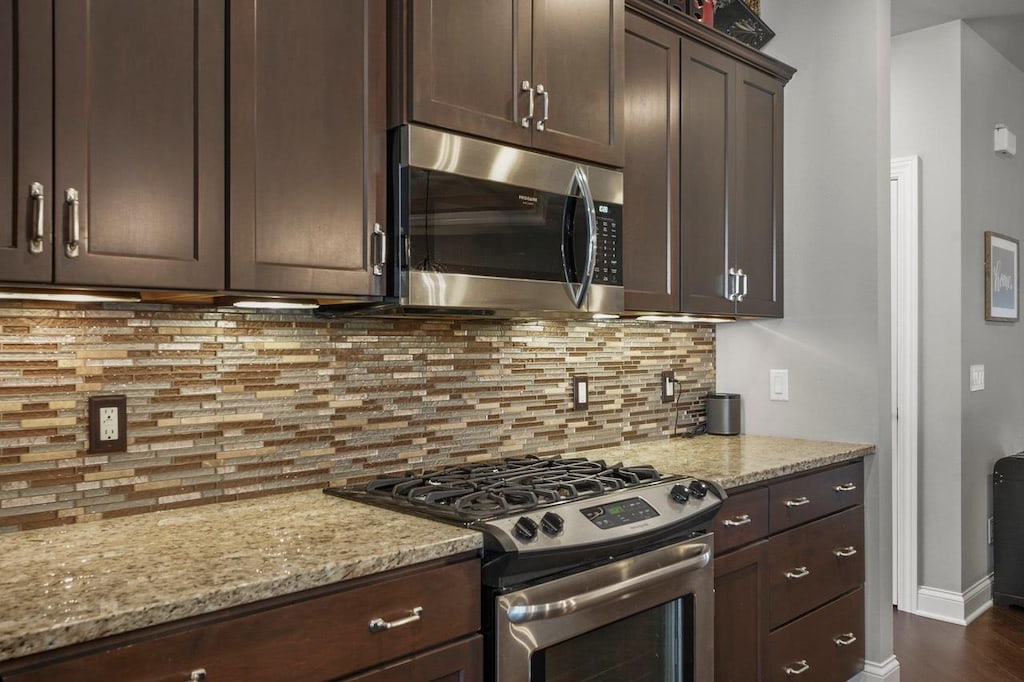 kitchen with dark brown cabinetry, stainless steel appliances, light stone counters, and tasteful backsplash