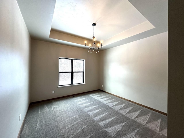 empty room featuring carpet, an inviting chandelier, and a tray ceiling