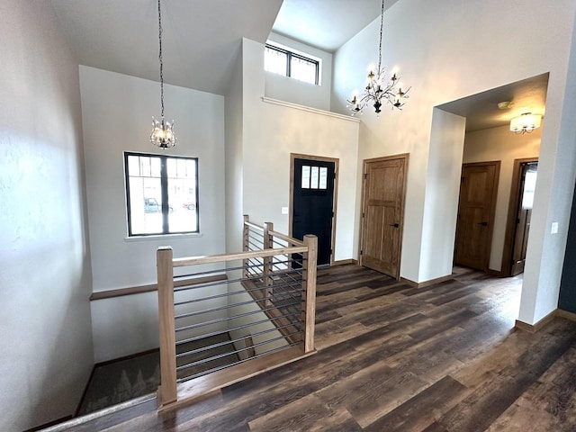 foyer entrance with a towering ceiling, dark wood-type flooring, and an inviting chandelier