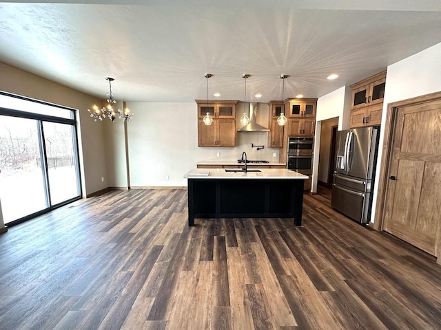 kitchen with appliances with stainless steel finishes, an island with sink, pendant lighting, and wall chimney range hood