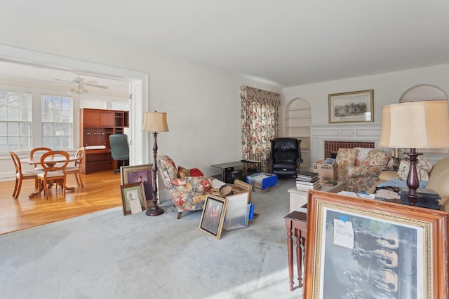 living room with built in shelves, light colored carpet, a brick fireplace, and ceiling fan