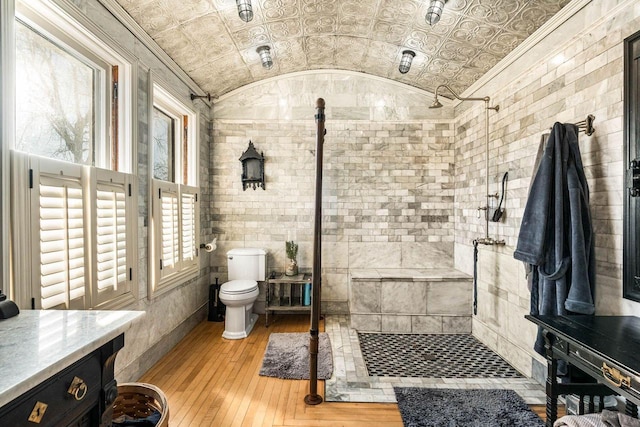 bathroom with a shower, a healthy amount of sunlight, vaulted ceiling, and brick ceiling