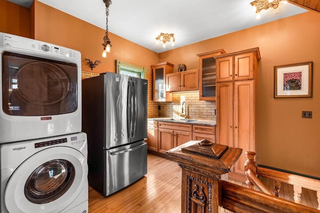 kitchen with stainless steel refrigerator, light stone countertops, stacked washer and clothes dryer, sink, and backsplash