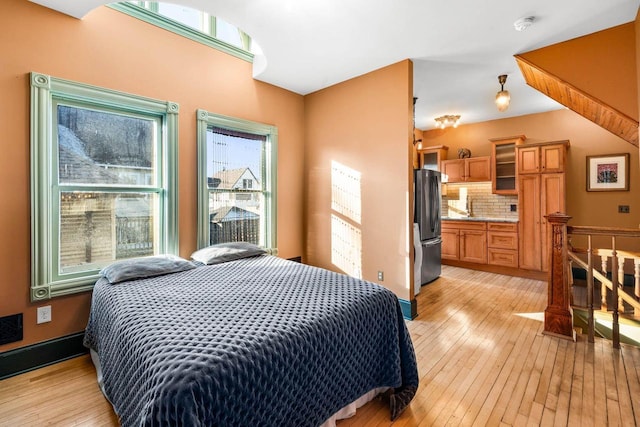 bedroom featuring connected bathroom, stainless steel refrigerator, and light hardwood / wood-style flooring