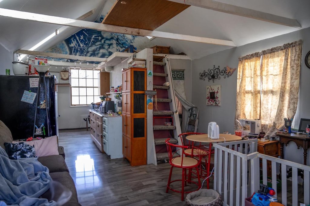 interior space with a nursery area, black fridge, wood-type flooring, and vaulted ceiling