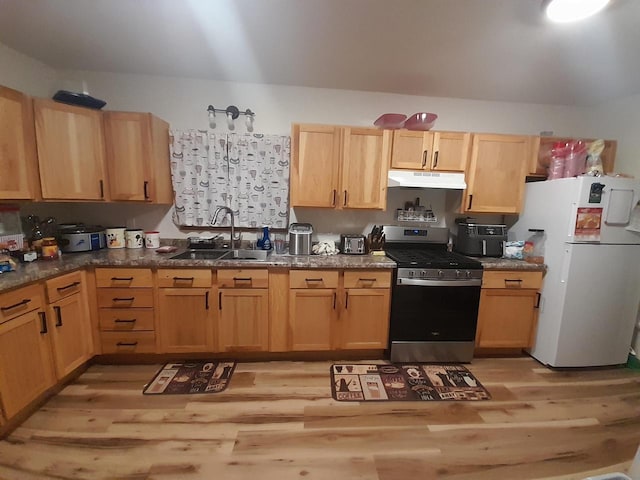 kitchen with under cabinet range hood, light brown cabinetry, freestanding refrigerator, stainless steel gas range, and a sink