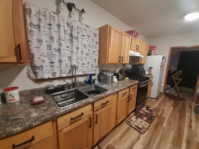 kitchen with sink, black range with gas stovetop, white fridge, dark stone counters, and light wood-type flooring