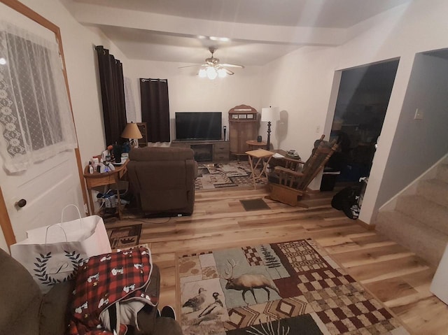 living area with beam ceiling, a ceiling fan, wood finished floors, and stairs