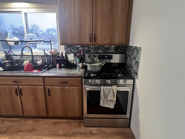 kitchen featuring sink, decorative backsplash, light wood-type flooring, and stainless steel gas stove