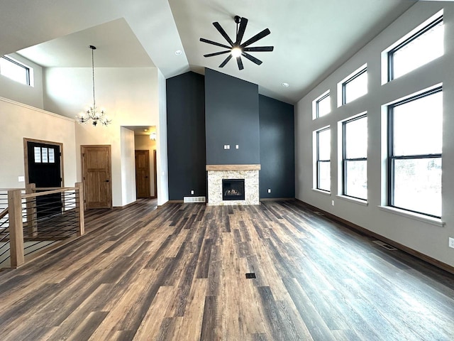 unfurnished living room featuring dark hardwood / wood-style flooring, a fireplace, a high ceiling, and ceiling fan with notable chandelier