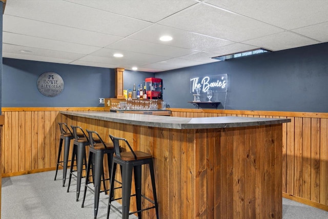 bar featuring a paneled ceiling, light carpet, and wood walls