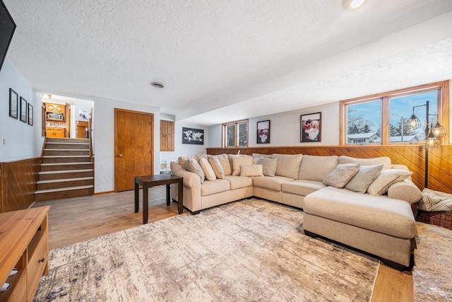 living room featuring a textured ceiling, wooden walls, and light hardwood / wood-style flooring