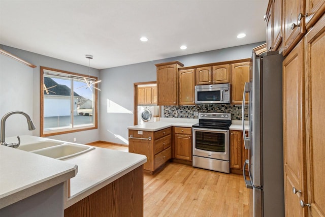 kitchen featuring sink, washer / clothes dryer, decorative light fixtures, appliances with stainless steel finishes, and light wood-type flooring