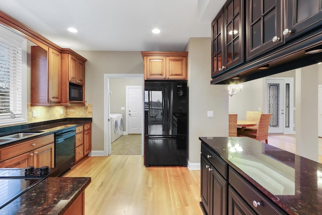 kitchen with dark stone counters, black appliances, sink, light wood-type flooring, and independent washer and dryer