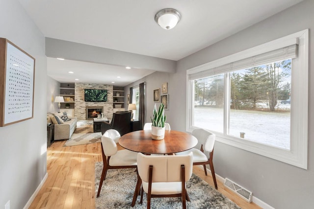 dining area with plenty of natural light, a large fireplace, built in features, and light wood-type flooring